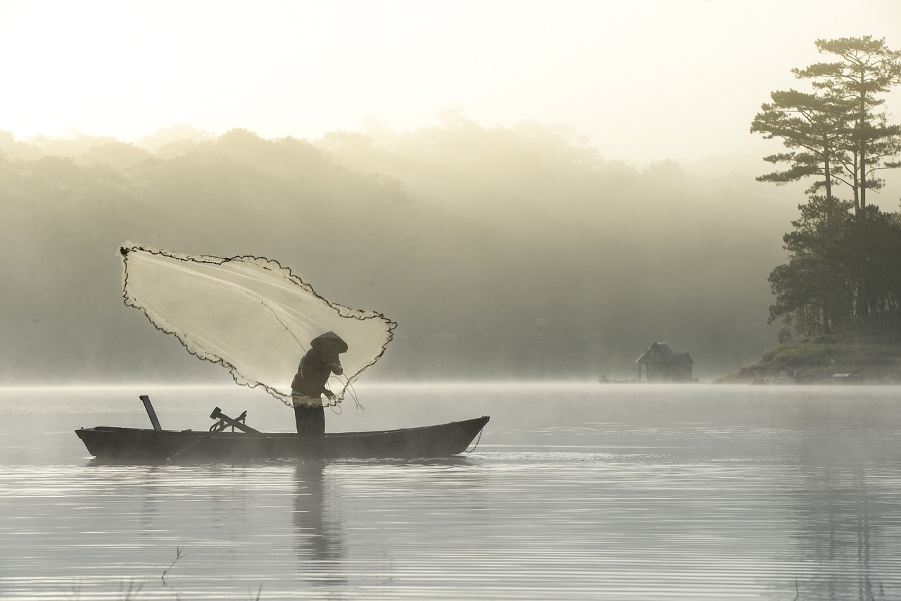 Pêcheur jetant son filet dans un lac du Vietnam, par météo brumeuse